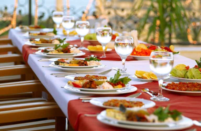 Delicious outdoor dinner party setup with elegant plates of food, wine glasses, and fresh salads on a long table with red and white tablecloths, perfect for sophisticated gatherings.