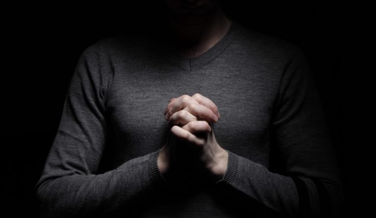 Praying person with hands clasped in dark lighting, symbolizing faith, hope, or contemplation.