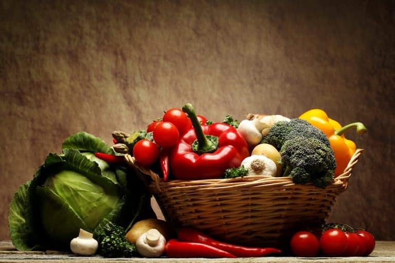 Fresh organic vegetables including red bell peppers, cherry tomatoes, broccoli, garlic, chili peppers, cabbage, and mushrooms in a woven basket, highlighting healthy eating and farm-to-table freshness.