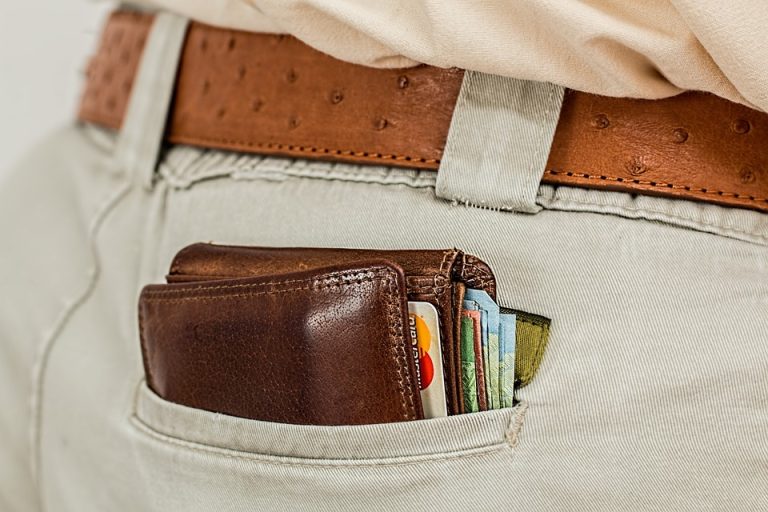 Wallet with credit cards and cash in the back pocket of beige pants, close-up shot.
