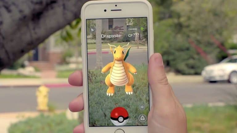 A person holding a smartphone capturing an augmented reality Dragonite from Pokémon GO outdoors on a clear day.