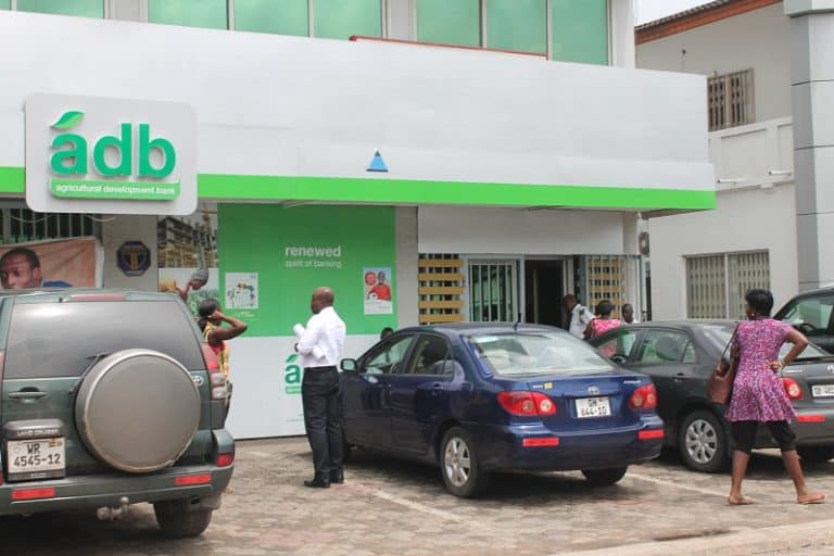 Bank of Agriculture Development (adb) branch with customers outside, outdoors in an urban setting, daytime, vehicles parked, showing banking services and customer interactions.