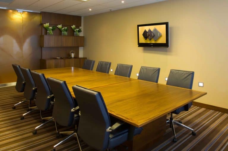 Modern conference room with wooden table and leather chairs, equipped for business meetings, interior design with mounted screen and decorative plants, perfect for corporate events and team collaboration.
